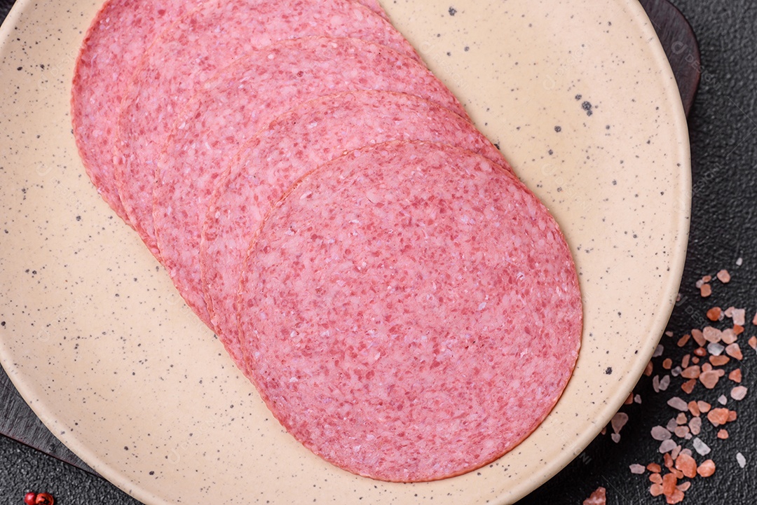Deliciosa salsicha de salame fumado com sal, especiarias e ervas cortadas em fatias sobre um fundo escuro de concreto