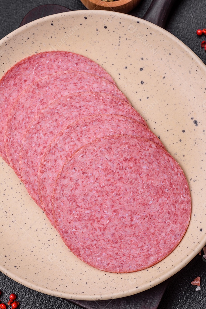 Deliciosa salsicha de salame fumado com sal, especiarias e ervas cortadas em fatias sobre um fundo escuro de concreto