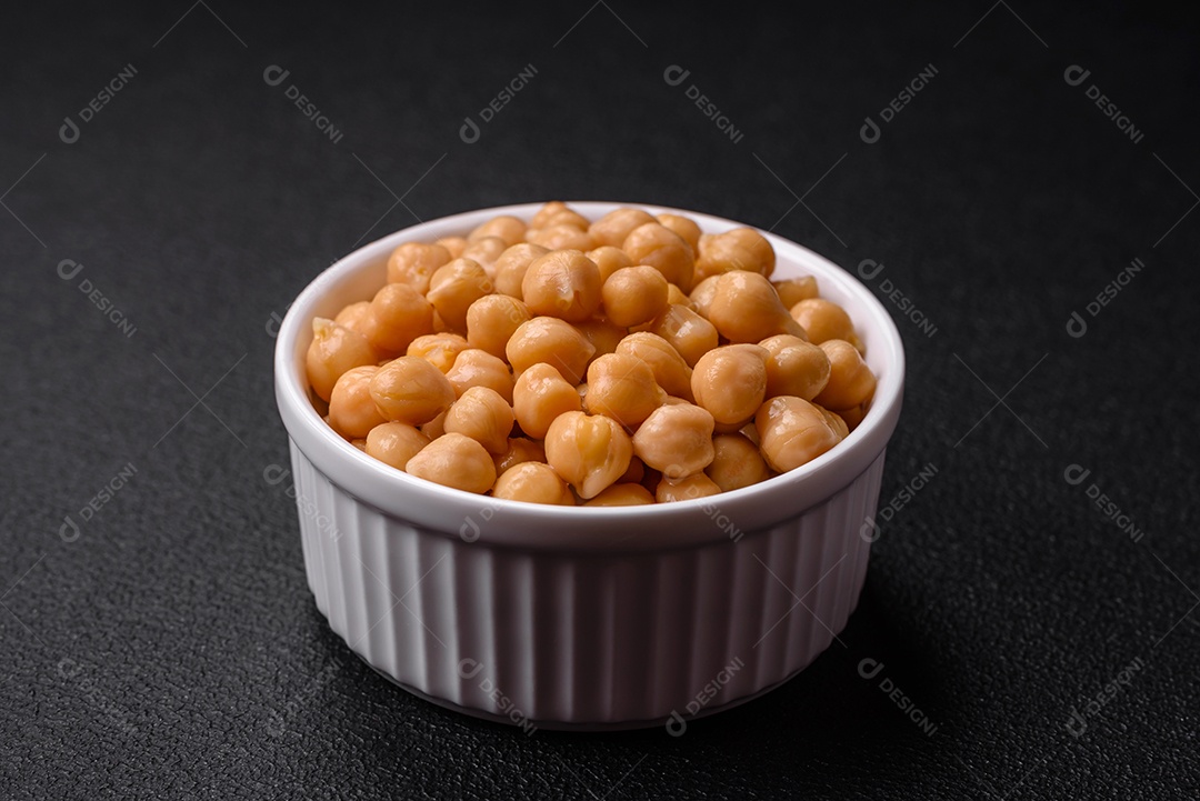 Delicioso grão de bico enlatado em um prato de cerâmica sobre um fundo escuro de concreto. Ingrediente para pratos vegetarianos