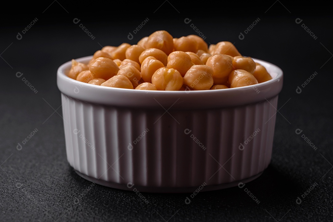 Delicioso grão de bico enlatado em um prato de cerâmica sobre um fundo escuro de concreto. Ingrediente para pratos vegetarianos