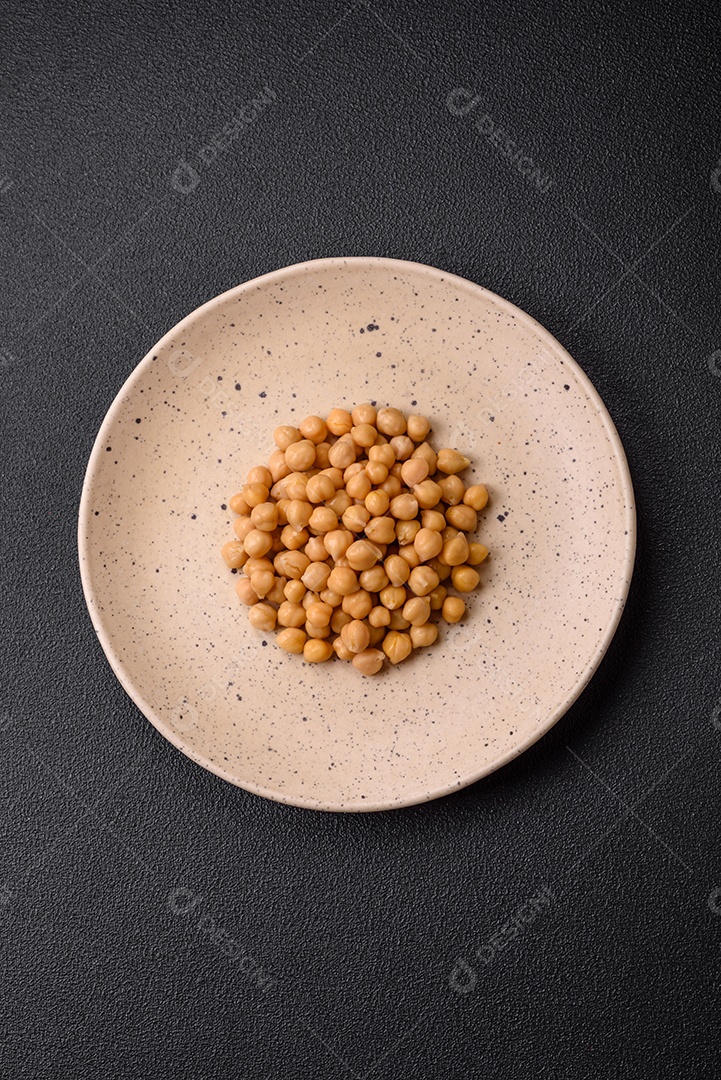 Delicioso grão de bico enlatado em um prato de cerâmica sobre um fundo escuro de concreto. Ingrediente para pratos vegetarianos