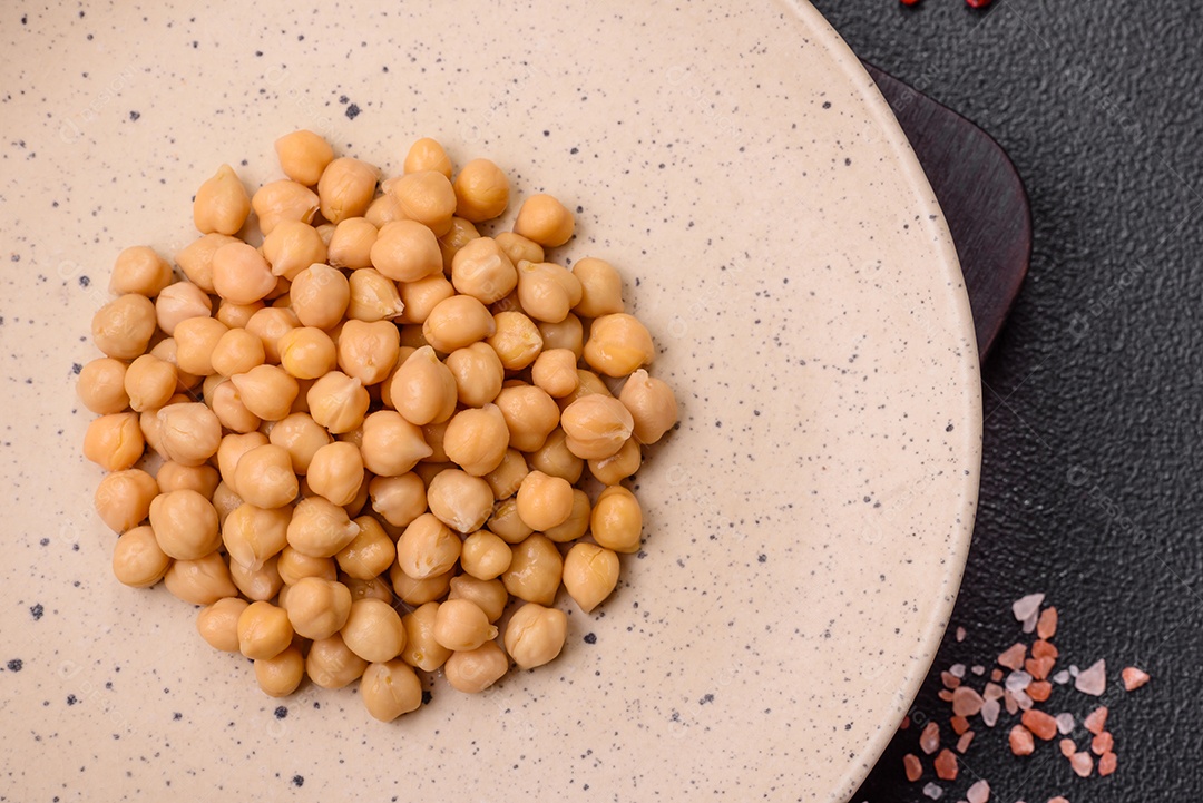 Delicioso grão de bico enlatado em um prato de cerâmica sobre um fundo escuro de concreto. Ingrediente para pratos vegetarianos