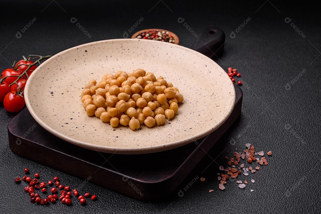 Delicioso grão de bico enlatado em um prato de cerâmica sobre um fundo escuro de concreto. Ingrediente para pratos vegetarianos