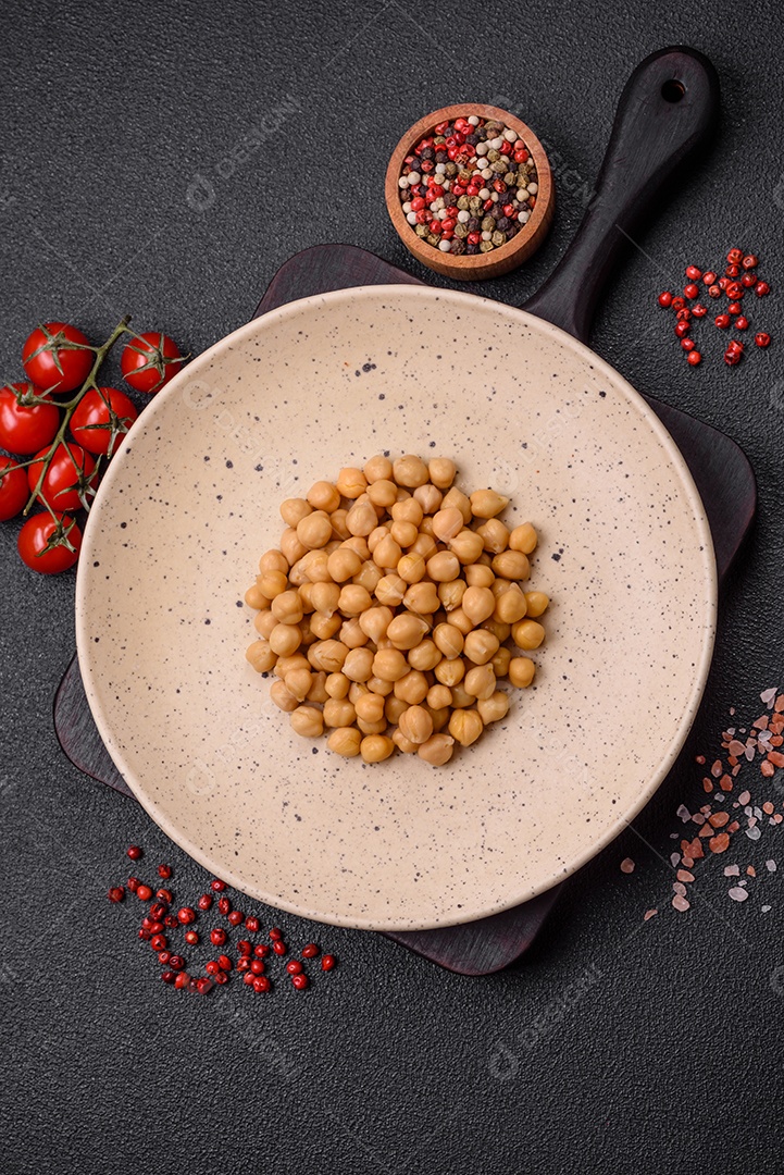 Delicioso grão de bico enlatado em um prato de cerâmica sobre um fundo escuro de concreto. Ingrediente para pratos vegetarianos