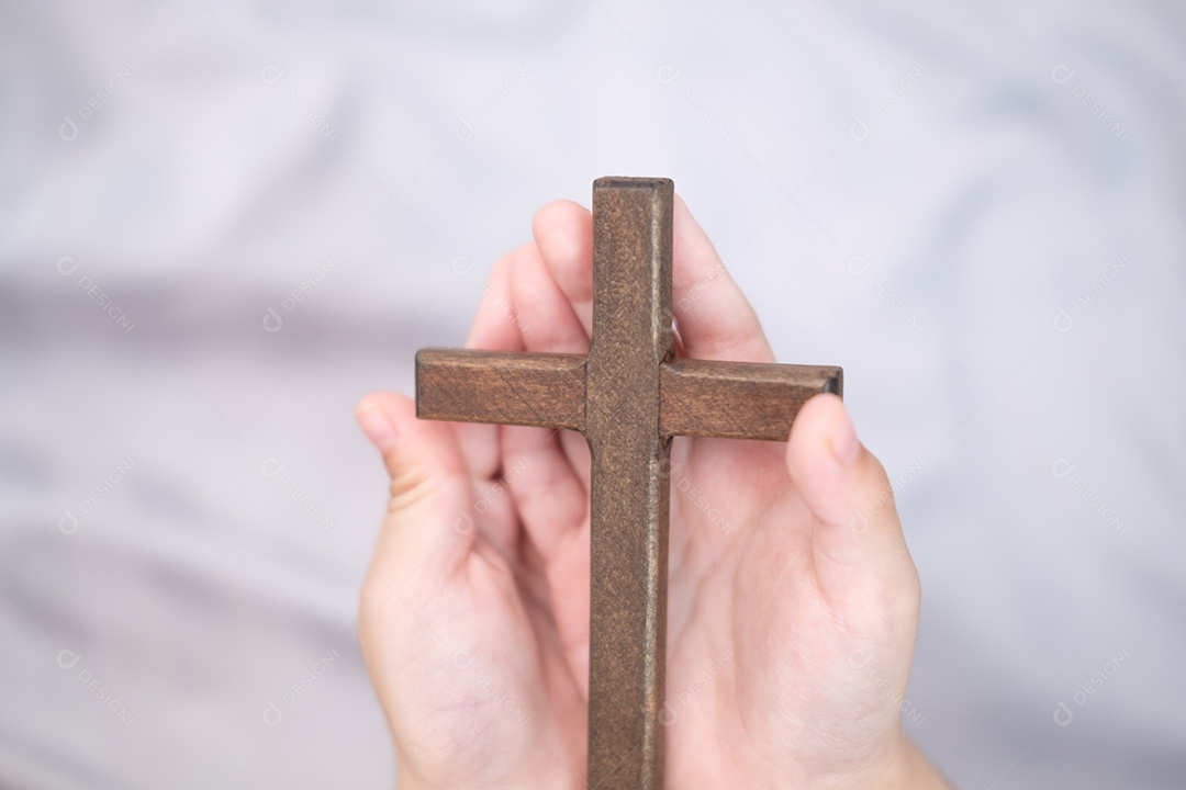 As mãos do menino estão segurando uma cruz