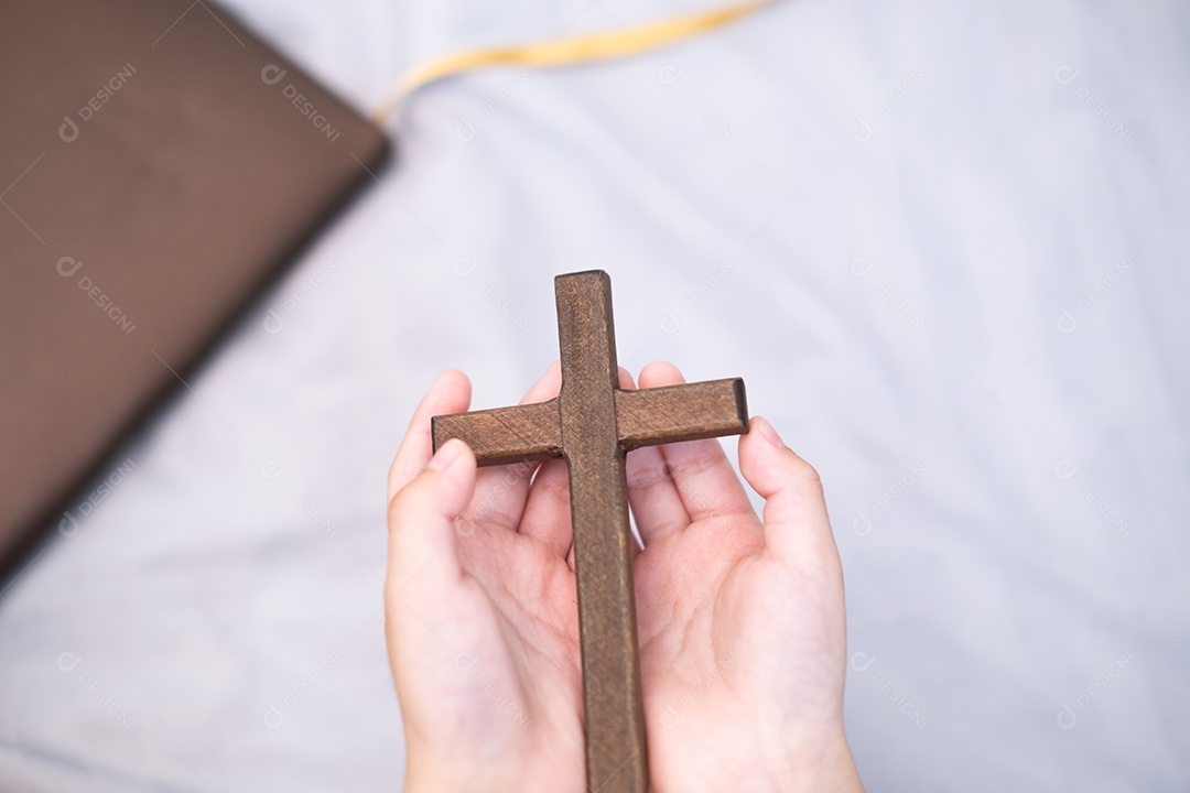 As mãos do menino estão segurando uma cruz