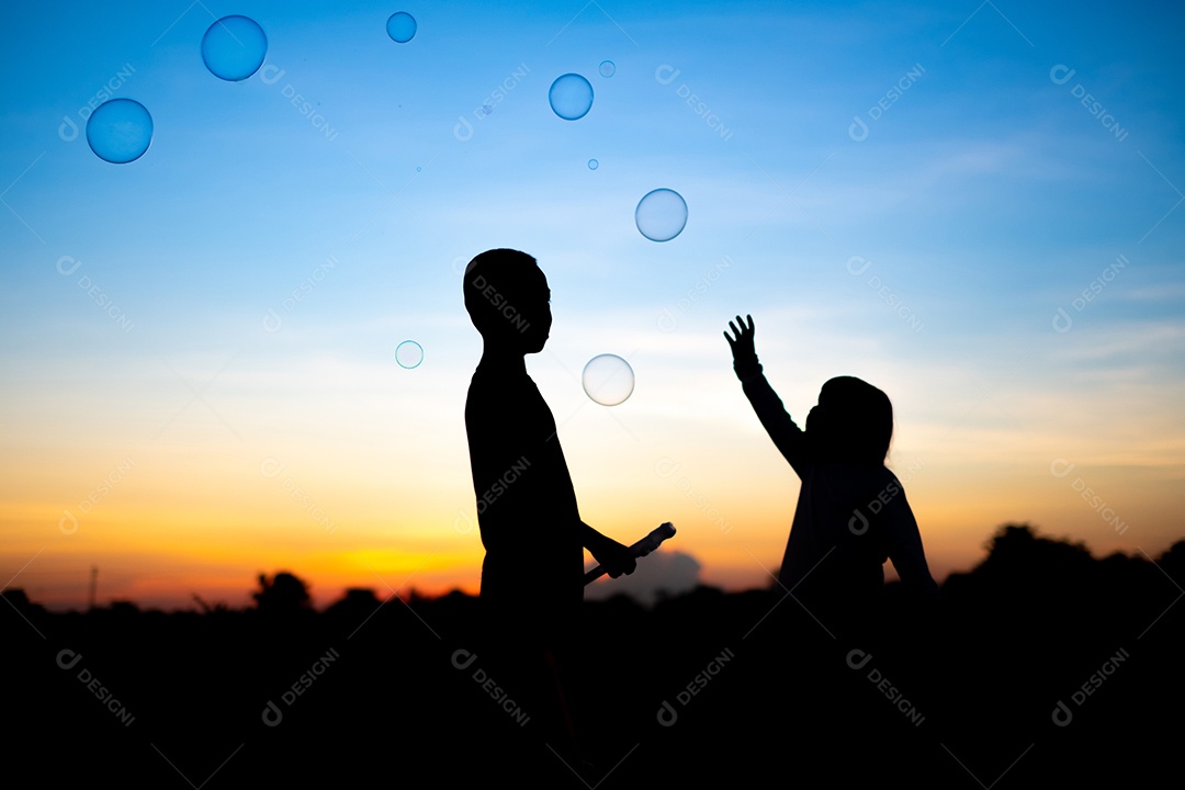 Silhueta de crianças exuberantes deliciando-se com um balão de água e um fundo dourado do pôr do sol