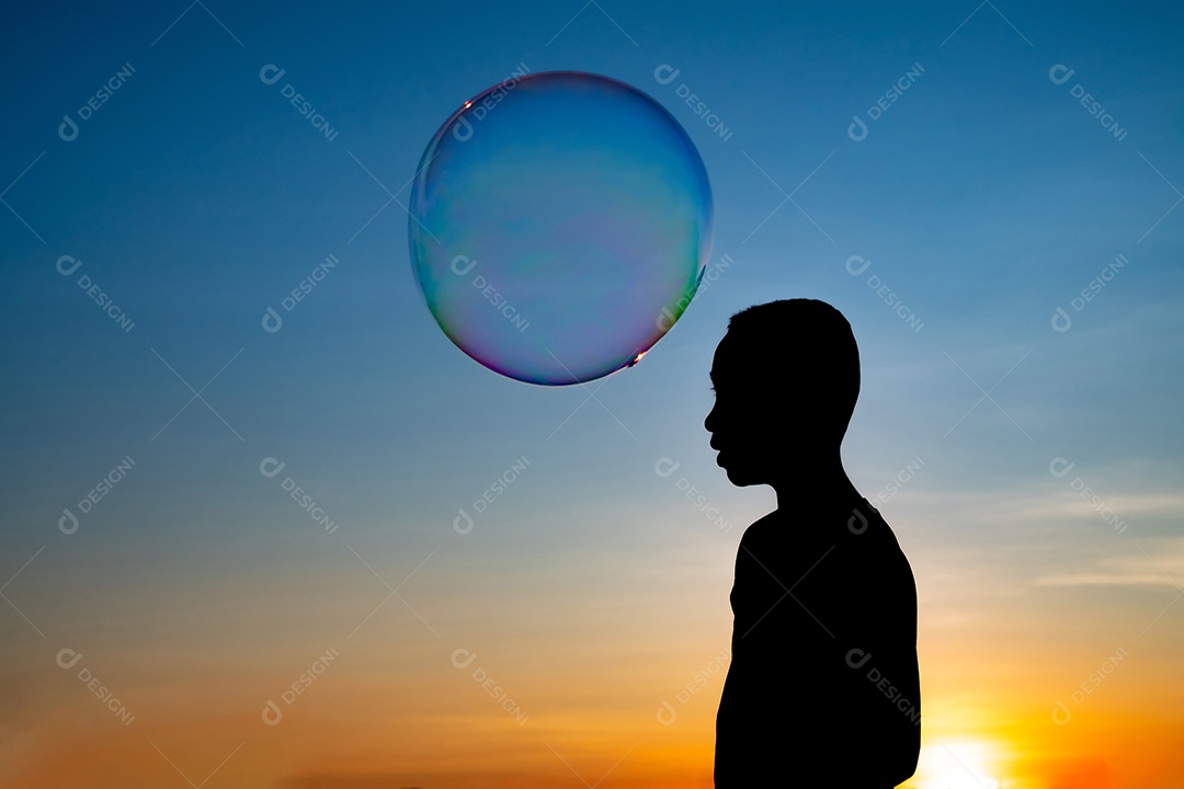 Silhueta de crianças exuberantes deliciando-se com um balão de água e um fundo dourado do pôr do sol