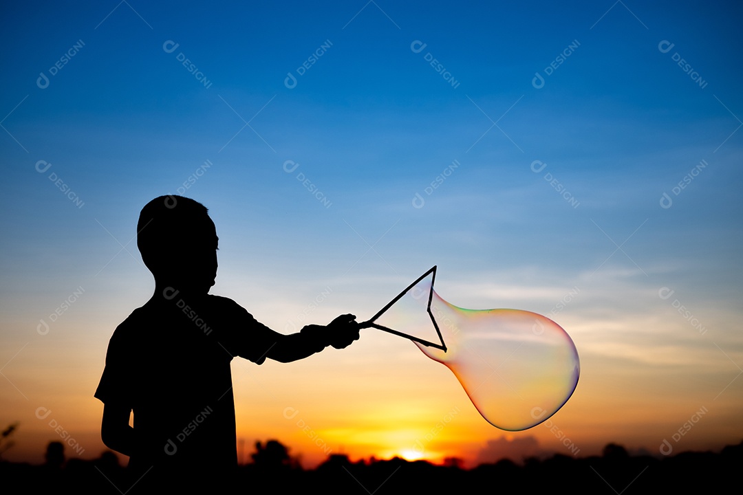 Silhueta de crianças exuberantes deliciando-se com um balão de água e um fundo dourado do pôr do sol