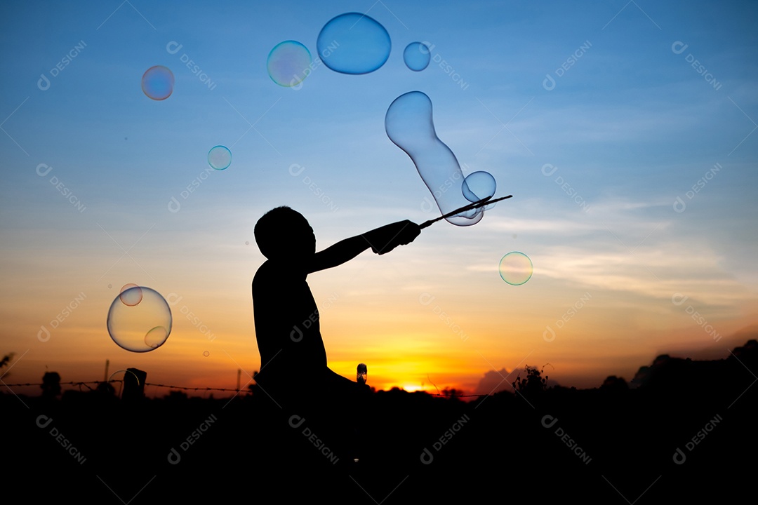 Silhueta de crianças exuberantes deliciando-se com um balão de água e um fundo dourado do pôr do sol