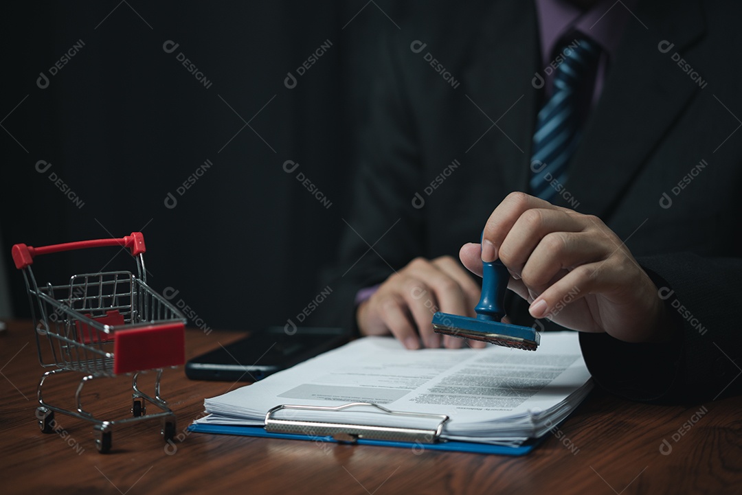 Mão de homem carimbando aprovação assinando contrato de documento ou papelada na mesa.