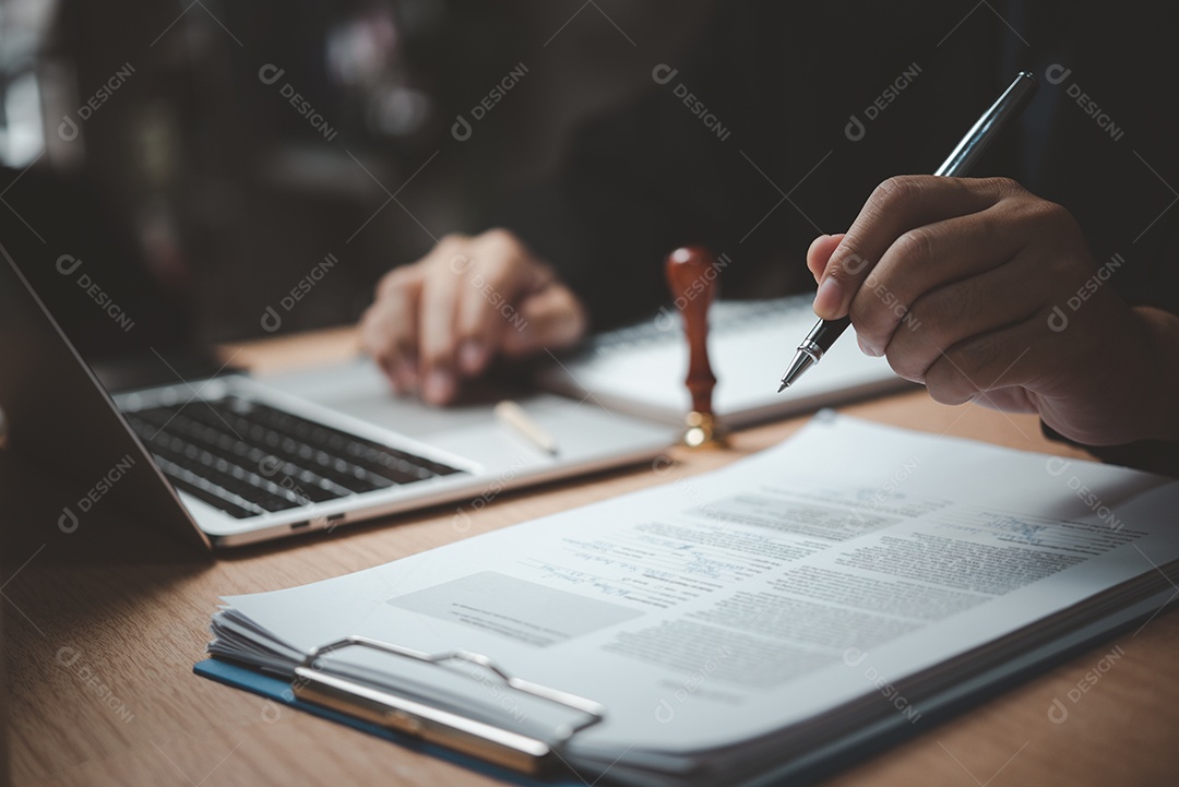 Mão de homem carimbando aprovação assinando contrato de documento ou papelada na mesa.