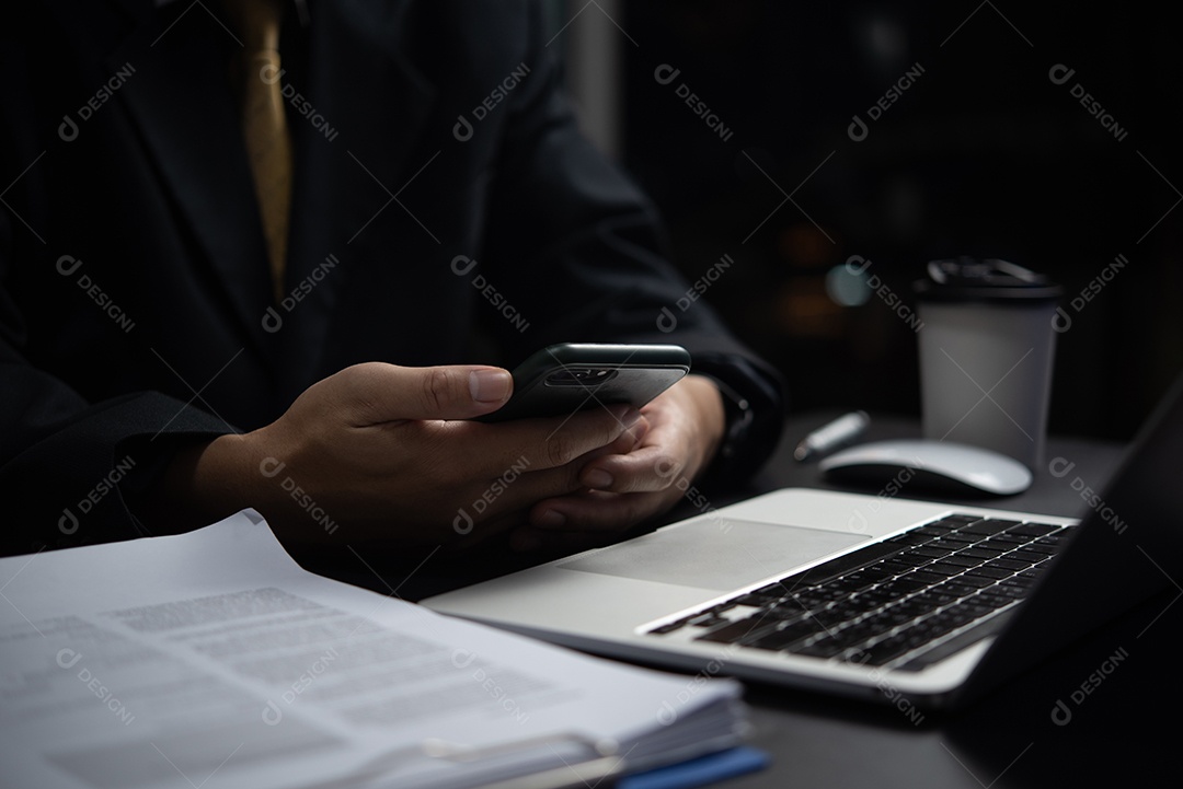 Empresário verificando documentos comerciais no telefone e no computador.