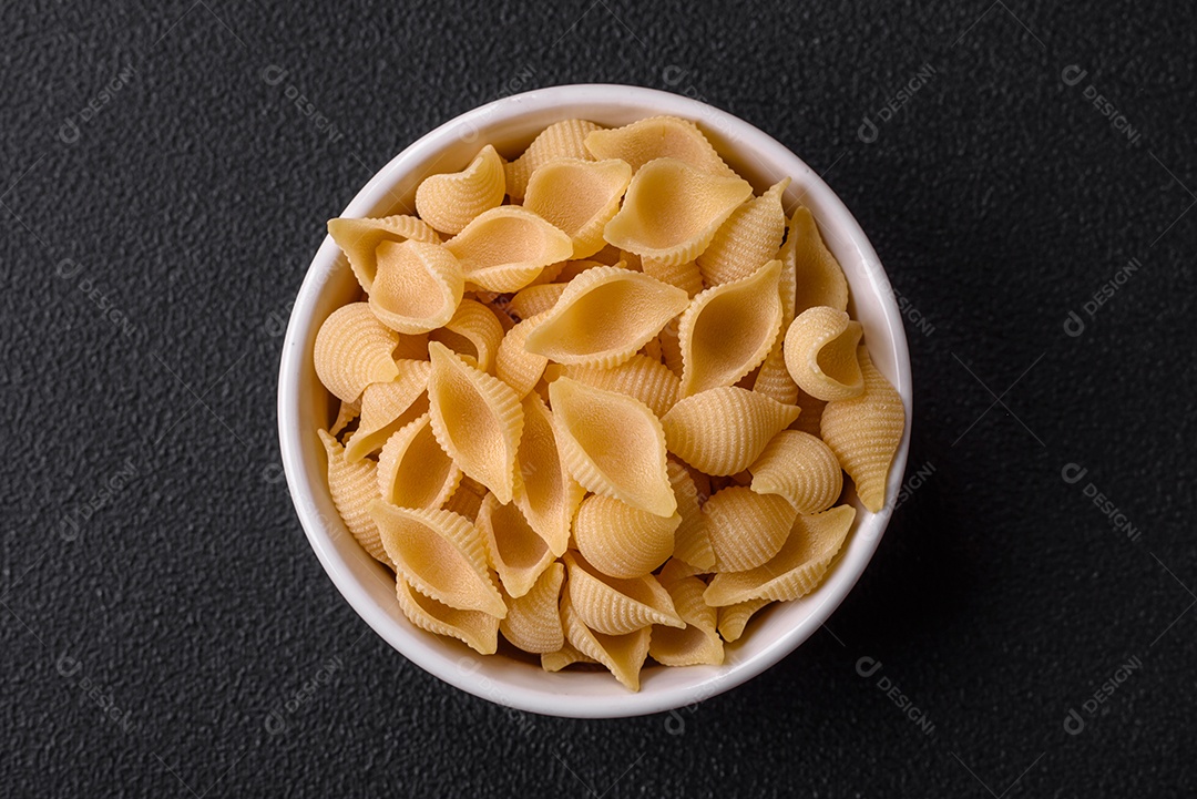 Conchiglie de massa italiana crua de trigo duro com legumes, sal e especiarias sobre um fundo escuro de concreto