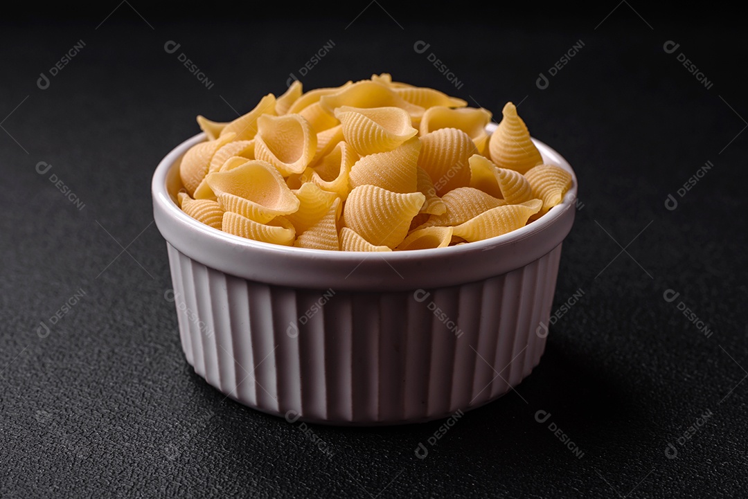 Conchiglie de massa italiana crua de trigo duro com legumes, sal e especiarias sobre um fundo escuro de concreto