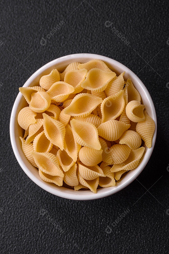 Conchiglie de massa italiana crua de trigo duro com legumes, sal e especiarias sobre um fundo escuro de concreto