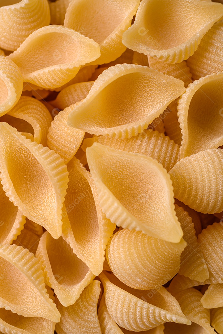 Conchiglie de massa italiana crua de trigo duro com legumes, sal e especiarias sobre um fundo escuro de concreto