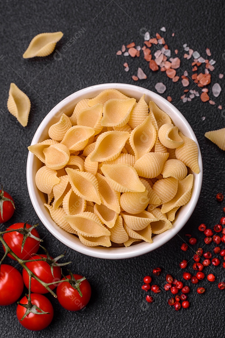 Conchiglie de massa italiana crua de trigo duro com legumes, sal e especiarias sobre um fundo escuro de concreto