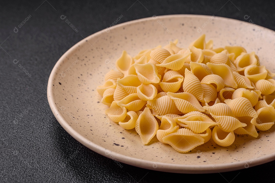Conchiglie de massa italiana crua de trigo duro com legumes, sal e especiarias sobre um fundo escuro de concreto
