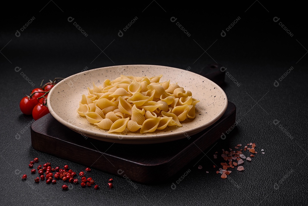 Conchiglie de massa italiana crua de trigo duro com legumes, sal e especiarias sobre um fundo escuro de concreto