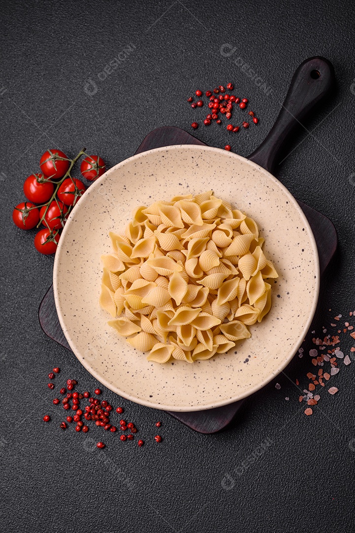 Conchiglie de massa italiana crua de trigo duro com legumes, sal e especiarias sobre um fundo escuro de concreto