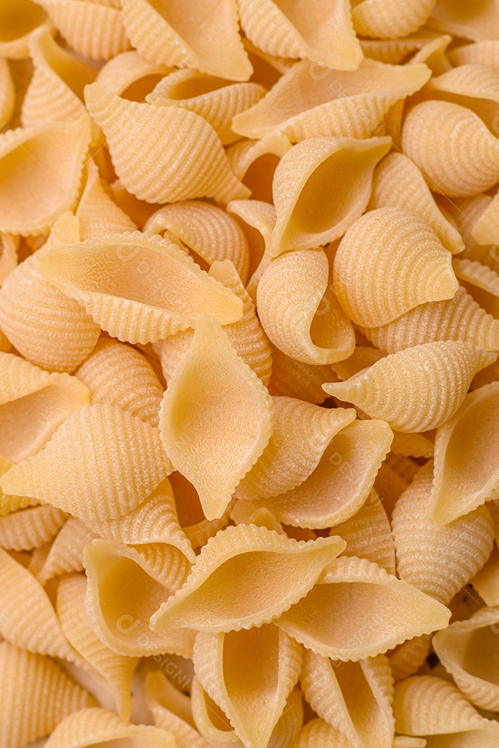 Conchiglie de massa italiana crua de trigo duro com legumes, sal e especiarias sobre um fundo escuro de concreto