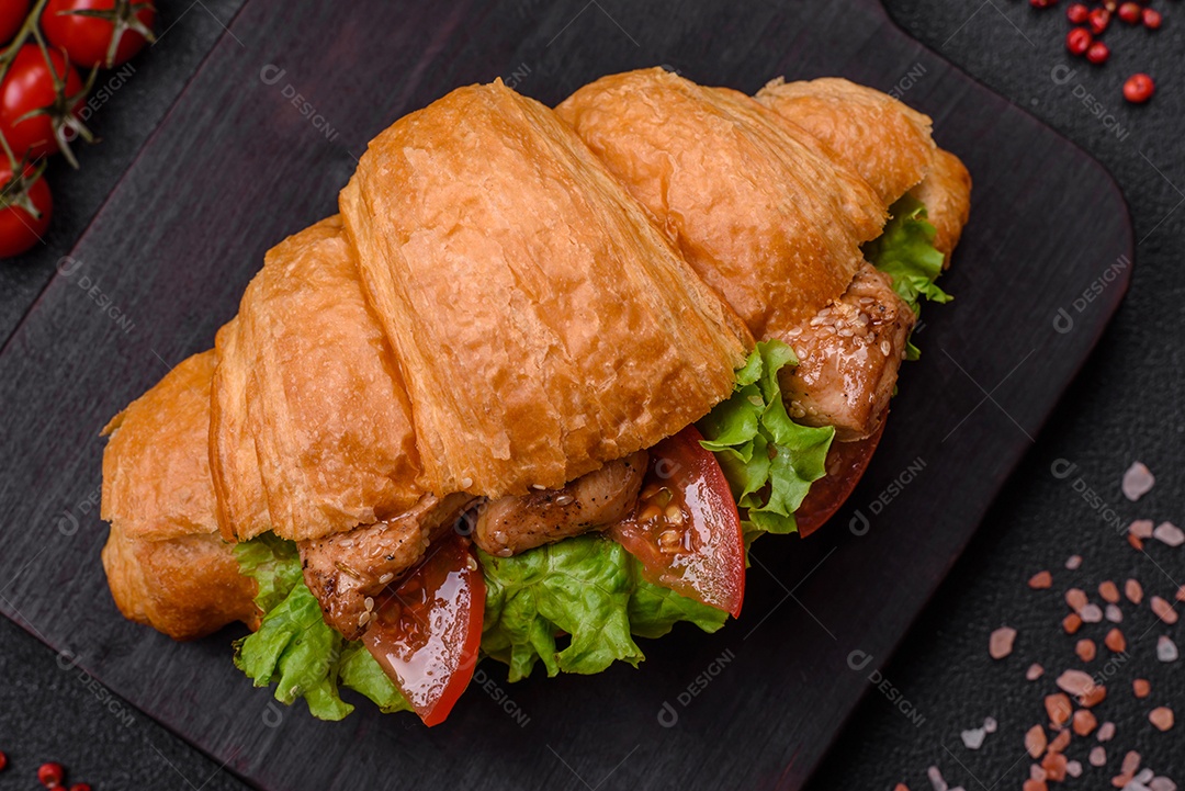Delicioso croissant crocante fresco com frango ou carne bovina, alface, tomate, especiarias e molho sobre um fundo escuro de concreto