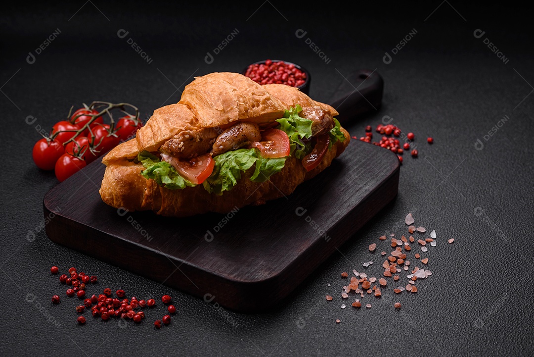 Delicioso croissant crocante fresco com frango ou carne bovina, alface, tomate, especiarias e molho sobre um fundo escuro de concreto