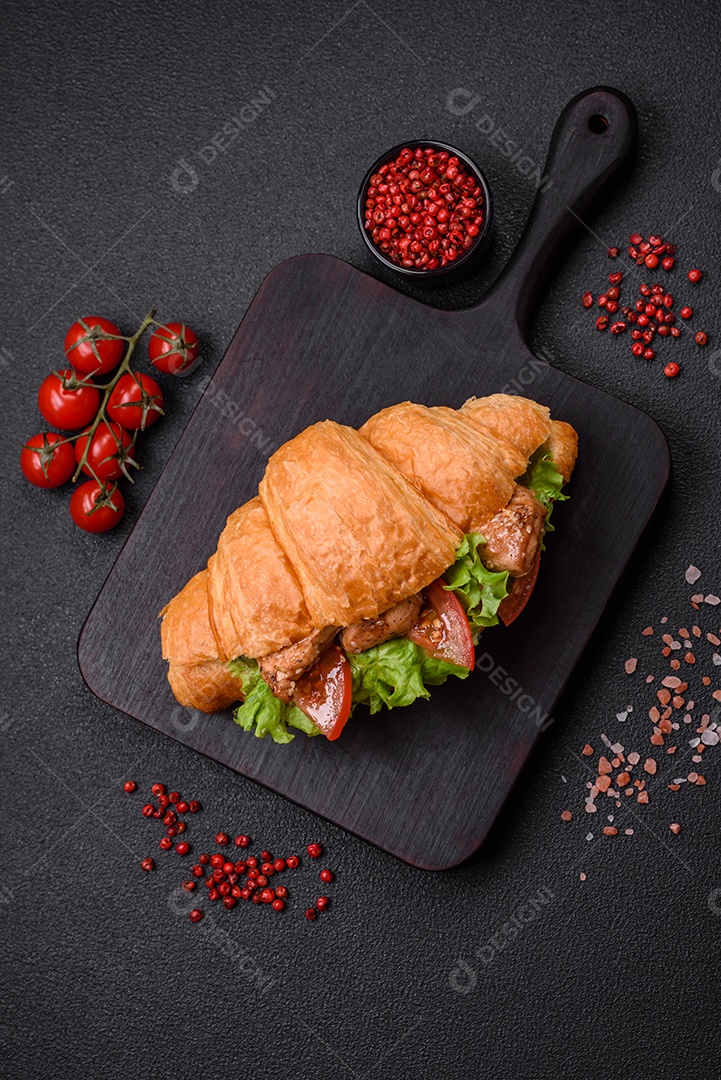 Delicioso croissant crocante fresco com frango ou carne bovina, alface, tomate, especiarias e molho sobre um fundo escuro de concreto