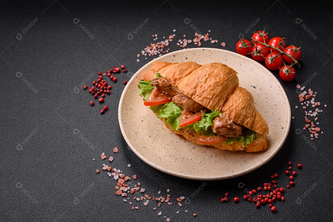 Delicioso croissant crocante fresco com frango ou carne bovina, alface, tomate, especiarias e molho sobre um fundo escuro de concreto