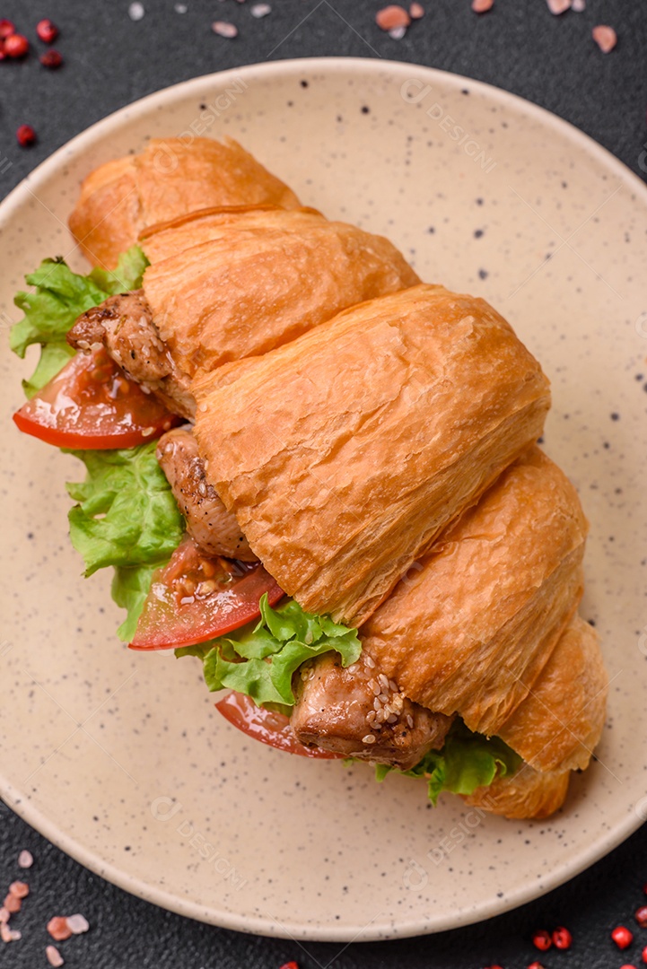 Delicioso croissant crocante fresco com frango ou carne bovina, alface, tomate, especiarias e molho sobre um fundo escuro de concreto