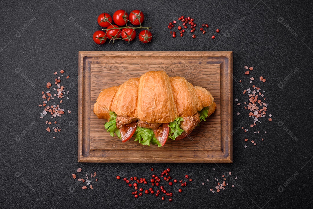 Delicioso croissant crocante fresco com frango ou carne bovina, alface, tomate, especiarias e molho sobre um fundo escuro de concreto