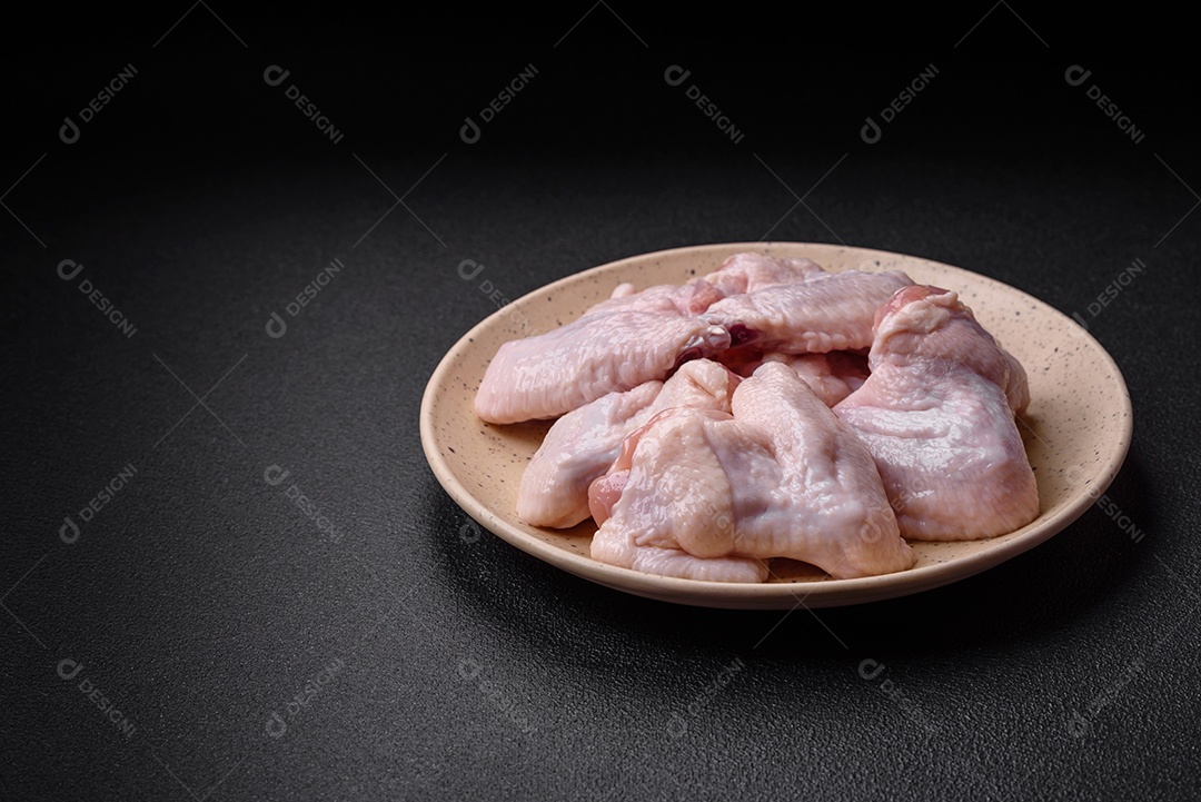 Asas de frango cruas frescas com sal e especiarias preparadas para assar sobre um fundo escuro de concreto