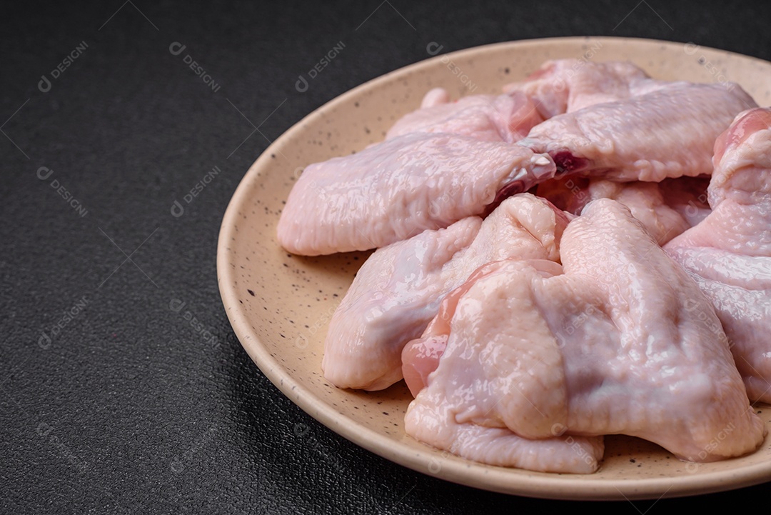 Asas de frango cruas frescas com sal e especiarias preparadas para assar sobre um fundo escuro de concreto