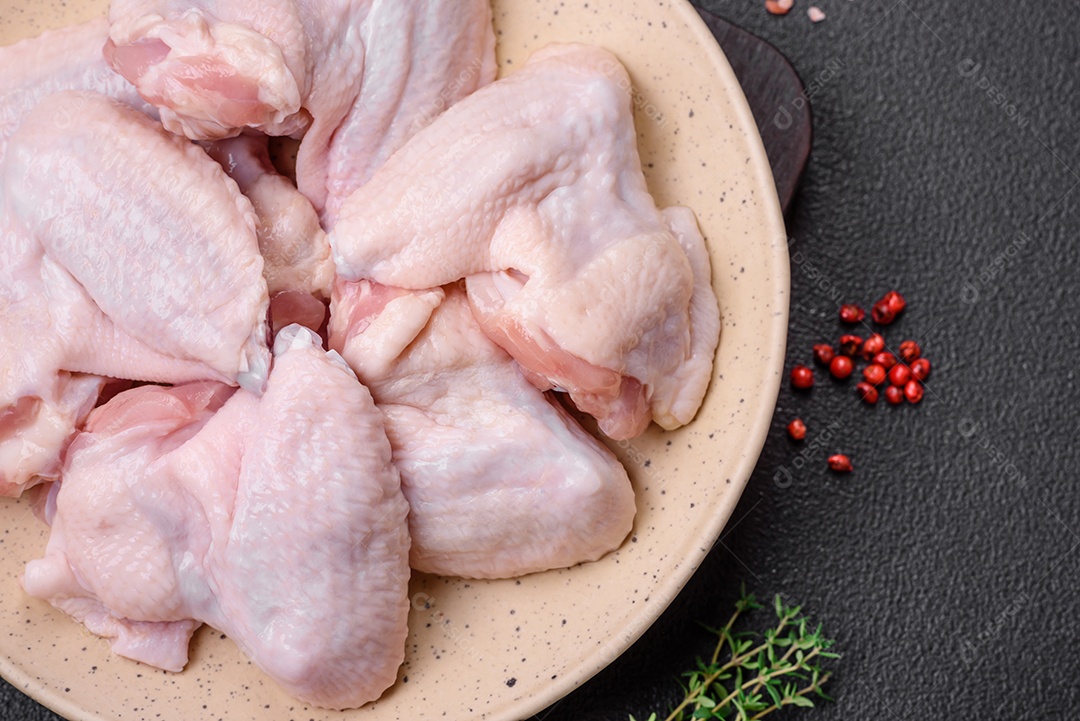 Asas de frango cruas frescas com sal e especiarias preparadas para assar sobre um fundo escuro de concreto