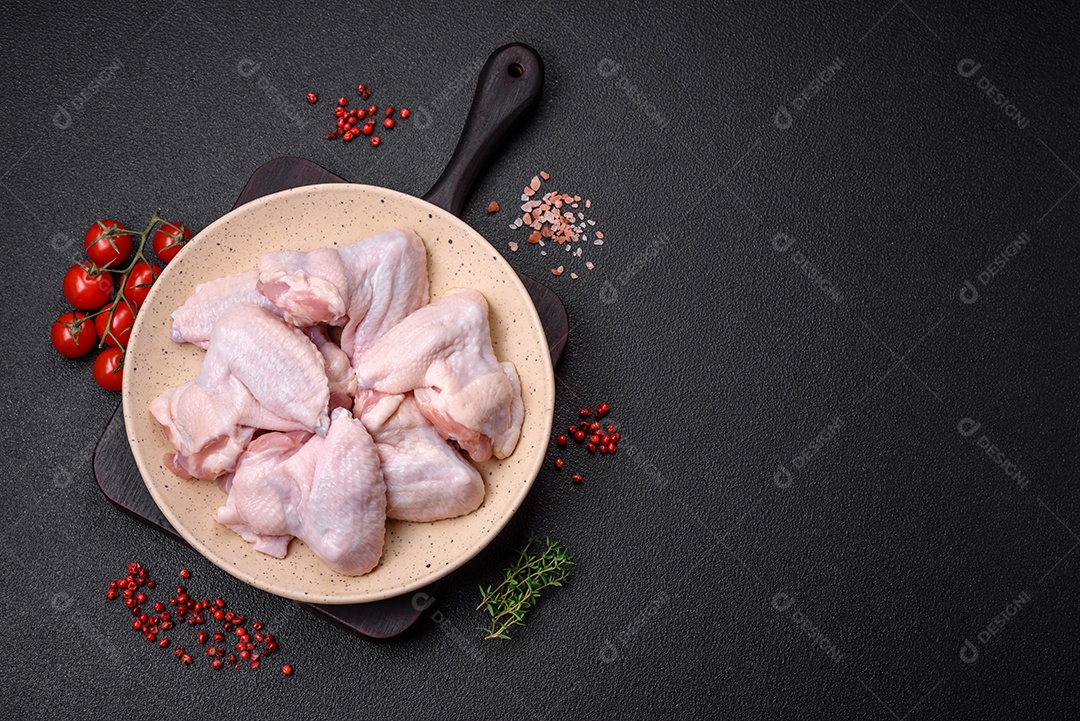 Asas de frango cruas frescas com sal e especiarias preparadas para assar sobre um fundo escuro de concreto