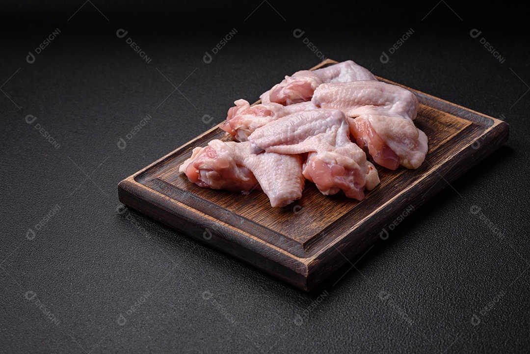 Asas de frango cruas frescas com sal e especiarias preparadas para assar sobre um fundo escuro de concreto