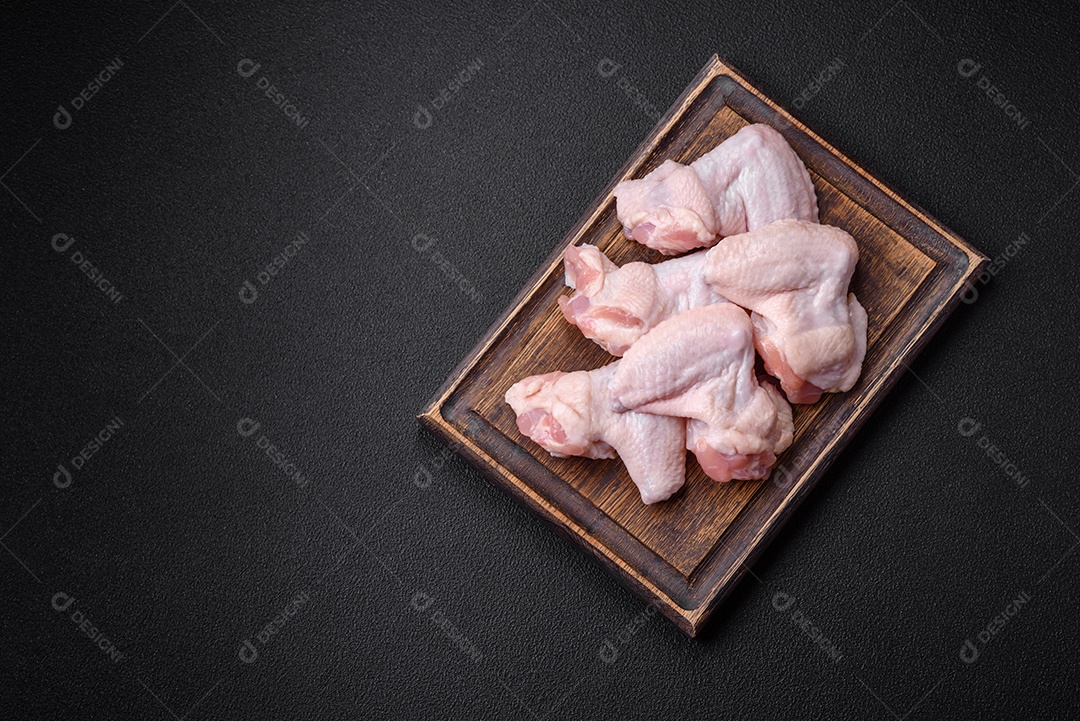 Asas de frango cruas frescas com sal e especiarias preparadas para assar sobre um fundo escuro de concreto