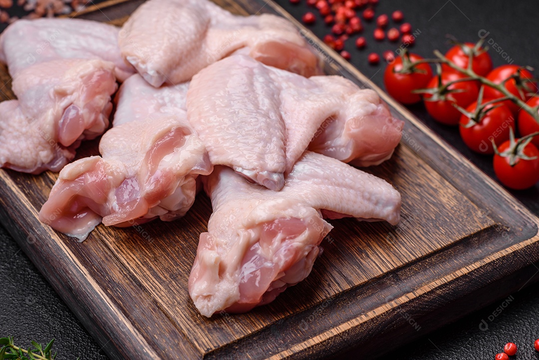 Asas de frango cruas frescas com sal e especiarias preparadas para assar sobre um fundo escuro de concreto