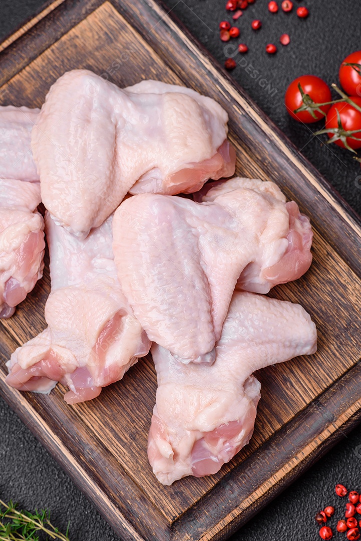 Asas de frango cruas frescas com sal e especiarias preparadas para assar sobre um fundo escuro de concreto