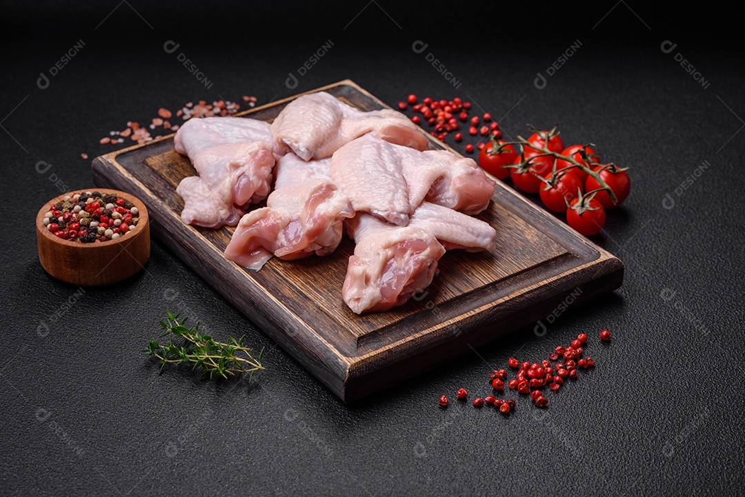 Asas de frango cruas frescas com sal e especiarias preparadas para assar sobre um fundo escuro de concreto