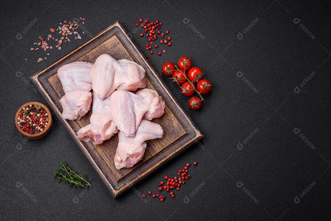 Asas de frango cruas frescas com sal e especiarias preparadas para assar sobre um fundo escuro de concreto