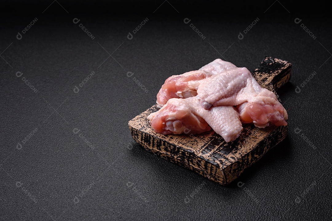 Asas de frango cruas frescas com sal e especiarias preparadas para assar sobre um fundo escuro de concreto