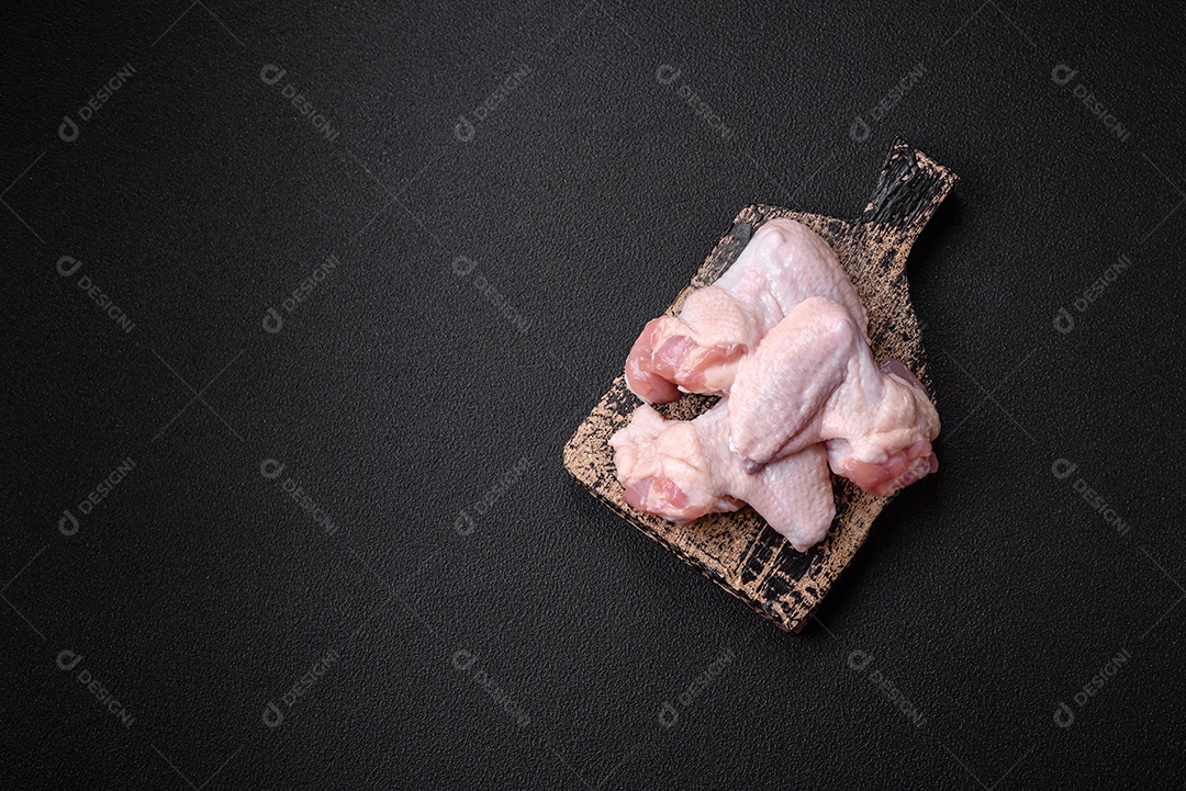 Asas de frango cruas frescas com sal e especiarias preparadas para assar sobre um fundo escuro de concreto
