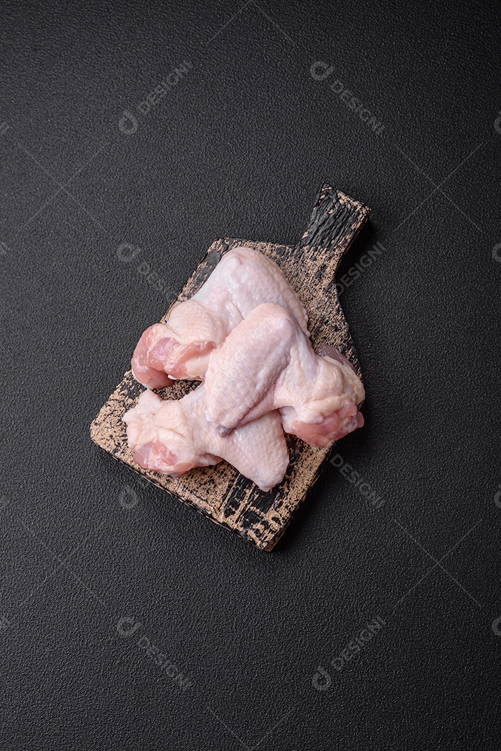 Asas de frango cruas frescas com sal e especiarias preparadas para assar sobre um fundo escuro de concreto