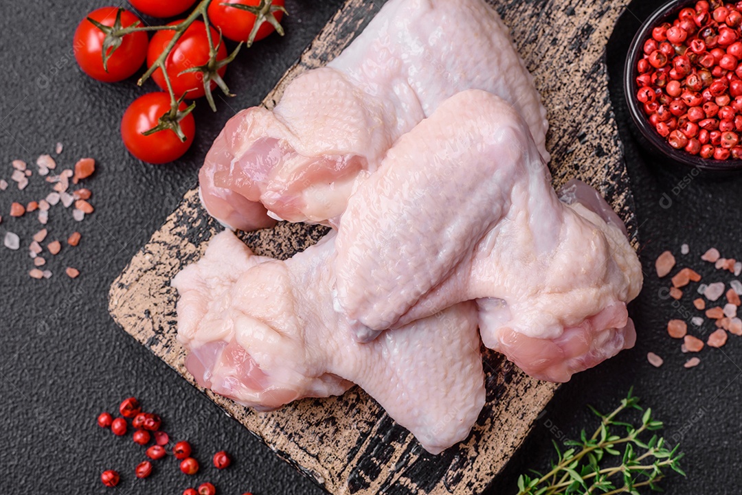 Asas de frango cruas frescas com sal e especiarias preparadas para assar sobre um fundo escuro de concreto