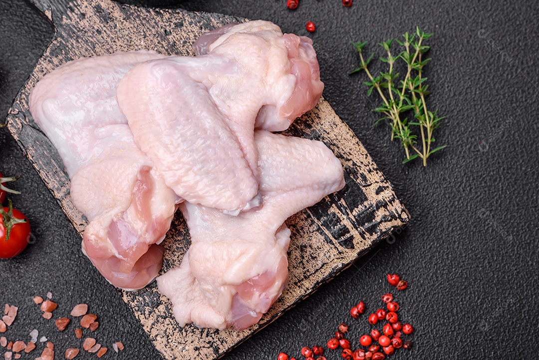 Asas de frango cruas frescas com sal e especiarias preparadas para assar sobre um fundo escuro de concreto