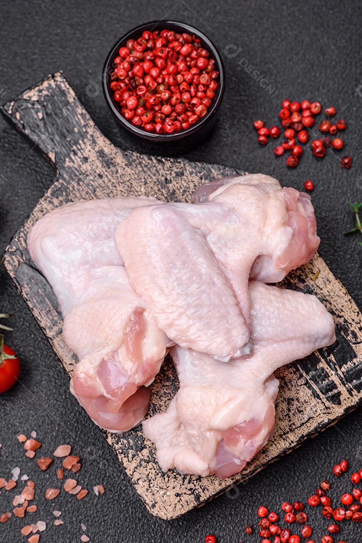 Asas de frango cruas frescas com sal e especiarias preparadas para assar sobre um fundo escuro de concreto