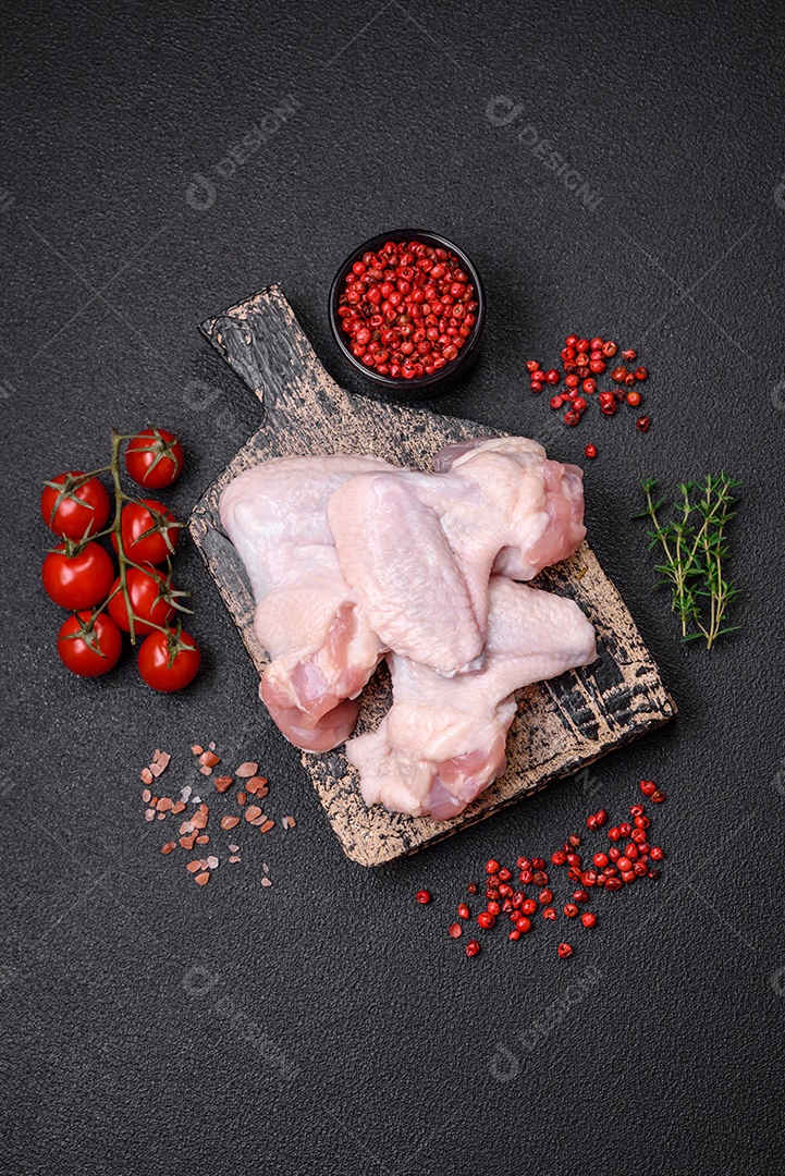 Asas de frango cruas frescas com sal e especiarias preparadas para assar sobre um fundo escuro de concreto
