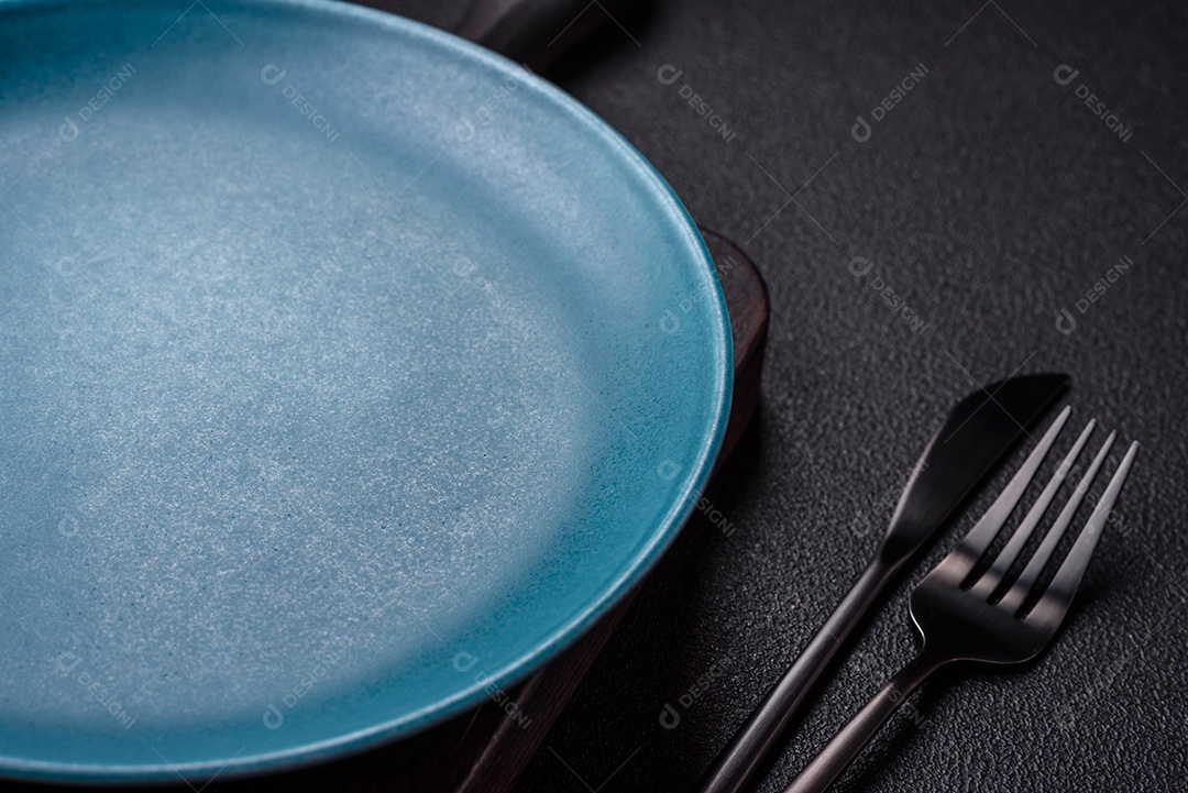 Linda placa cerâmica redonda vazia sobre um fundo de concreto. Utensílios de cozinha para servir comida na mesa